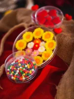 سه ظرف کریستالی گرد مغزی صدف پک در سایزهای مختلف، پر شده با پاستیل‌های رنگی گل و قلب و اسمارتیزهای ریز، که بر روی پارچه کنفی و ربان قرمز برای نمایش بسته‌بندی‌های هدیه و پذیرایی چیده شده‌اند.